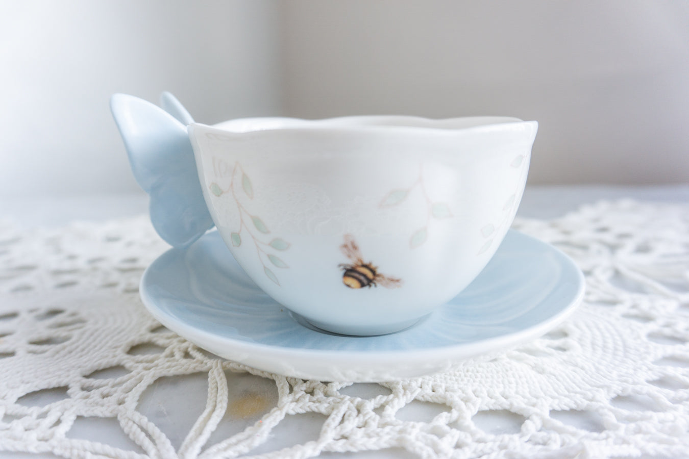 Lenox Butterfly Meadow blue porcelain tea cup with butterfly handle and matching saucer styled on a lace doily – whimsical spring tableware for cottagecore and garden-inspired decor.
