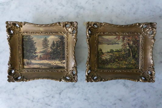 Two vintage miniature framed landscape prints with intricate, ornate frames, displayed on a marble surface.