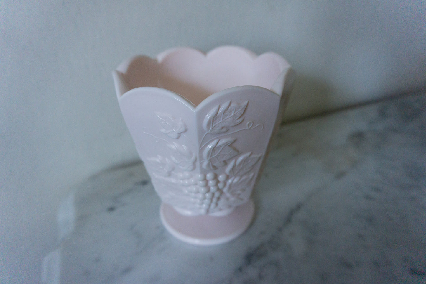 Close-up view of the embossed grape and vine pattern on the pink milk glass pedestal dish