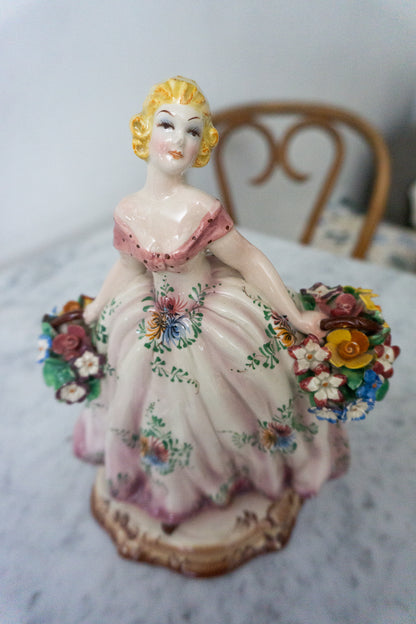 Front view of a porcelain figurine of a lady in a pink dress holding flower baskets