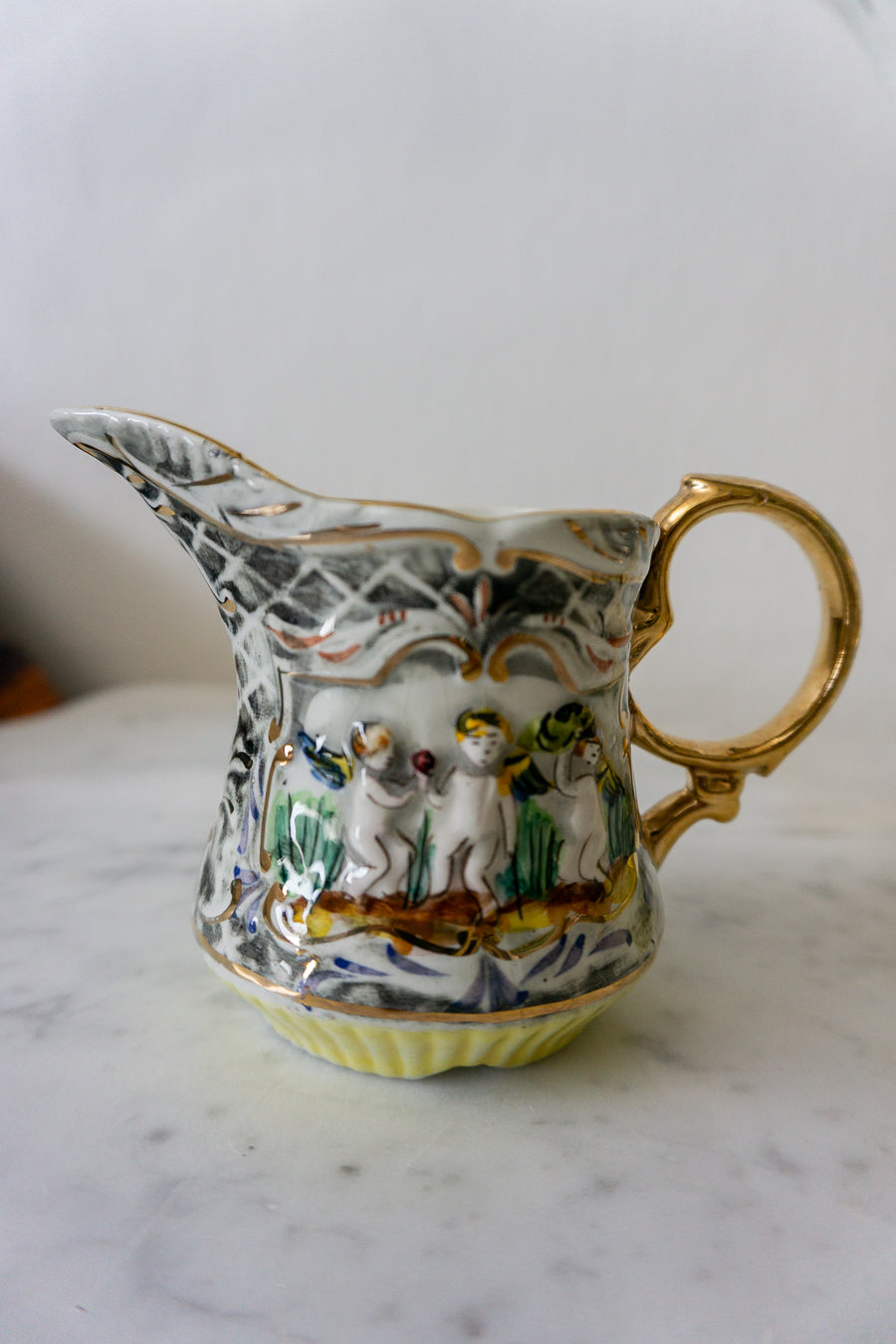 Side view of Pereiras Valado porcelain creamer with intricate hand-painted cherub design