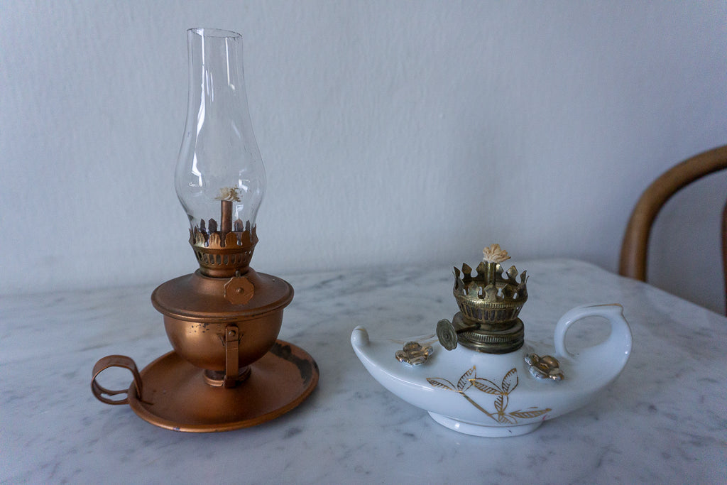 Copper finish miniature lamp with glass chimney and porcelain base on a marble surface.