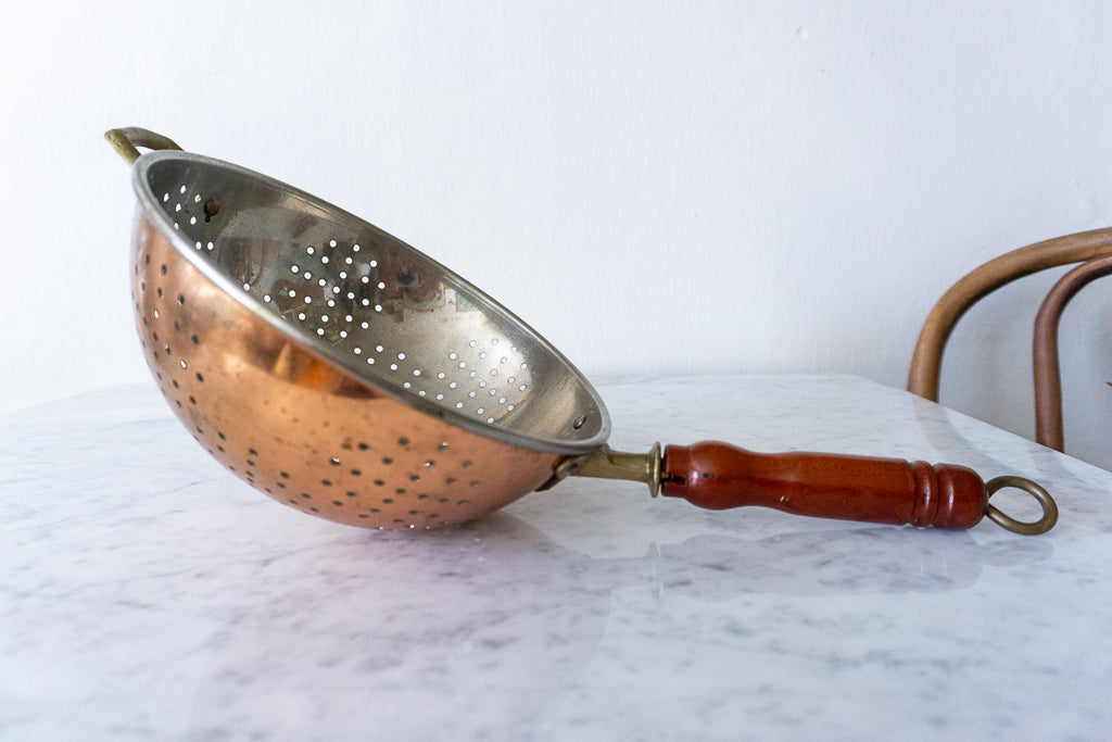 Vintage copper colander with a wooden handle.