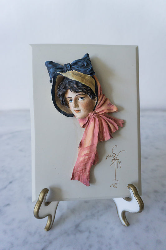 Hand-painted wall plaque "Anna" by Reco International, featuring a woman's portrait with a bonnet and pink scarf.