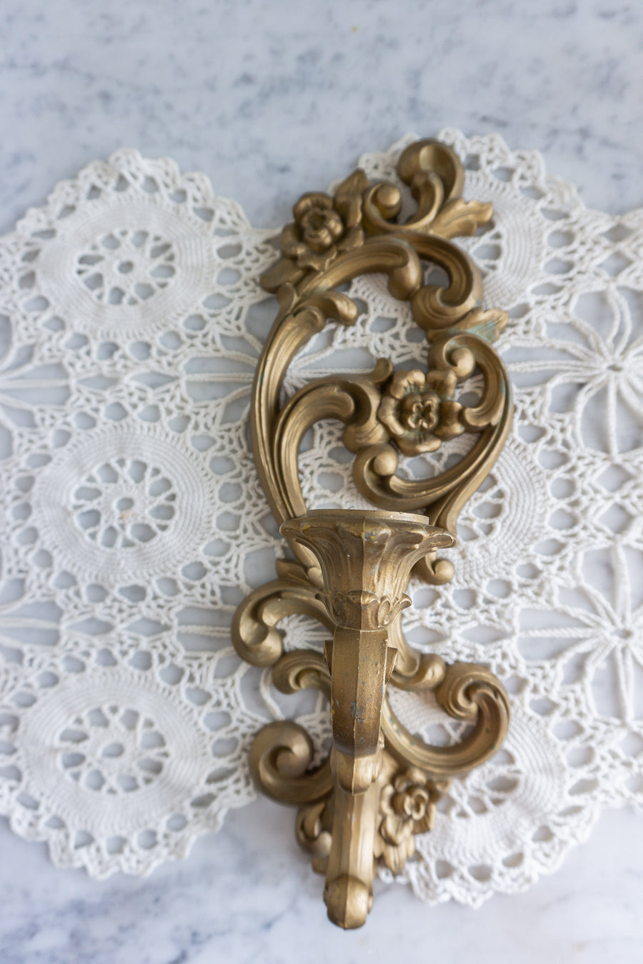 Ornate gold candle wall sconce with floral scrollwork on lace background
