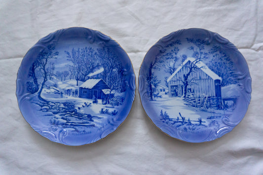 Blue and white decorative plates with winter scenes featuring a log cabin and homestead.